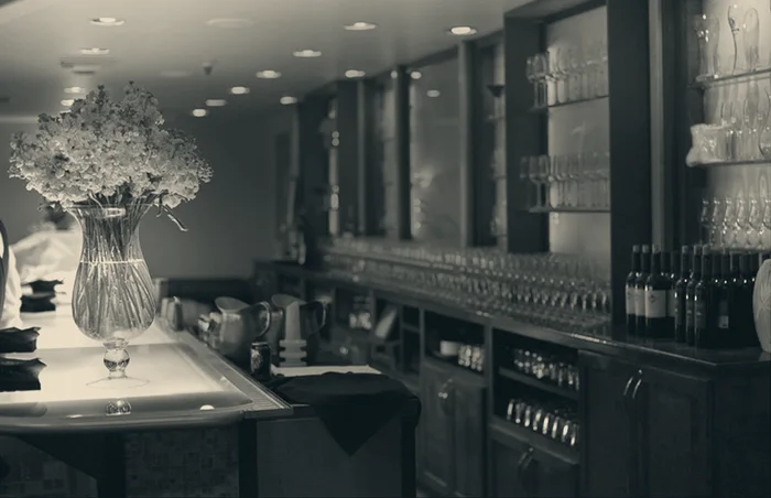 Archive photograph of a long bar with bottles on the back shelves and a vase of flowers on the counter.