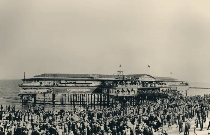 Archive photograph of a crowded Galveston beach in front of a large timber bathhouse pavilion.