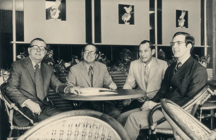 Archive photograph of four men in suits seated at a restaurant table in bentwood chairs.